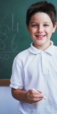 Portrait of cheerful school kid standing against chalkboard
